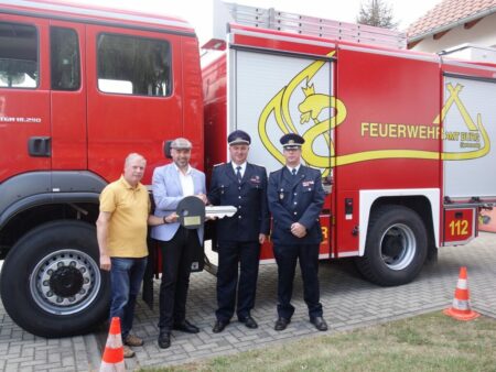 Joachim Dieke, Amtsdirektor Tobias Hentschel und Markus Weber übergeben den symbolischen Schlüssel an Ortswehrführer Uwe Bertels vor dem neuen Feuerwehrfahrzeug.