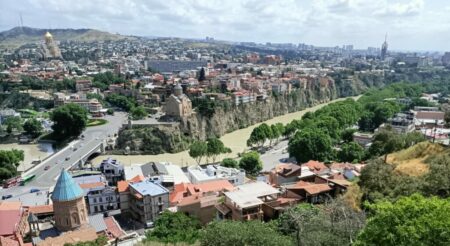 Spektakulärer Städtebau in Tbilisi: auf der hohen Felskante über dem Mtkwari-Fluss erhebt sich die Metechi Kirche (Bildmitte). Bauten späterer Zeiten kargen teils über den Felsrand hinaus. Ein typisch georgisches Kuriosum stellt die Sameba-Kathedrale (im Bild oben links) dar. Sie sieht alt aus, wurde aber erst 2004 geweiht, finanziert vom Milliardär Bidsina Iwanischwili, der 2012/13 Premierminister war. Diese größte aller Kirchen ist heute Residenz des Patriarchen.