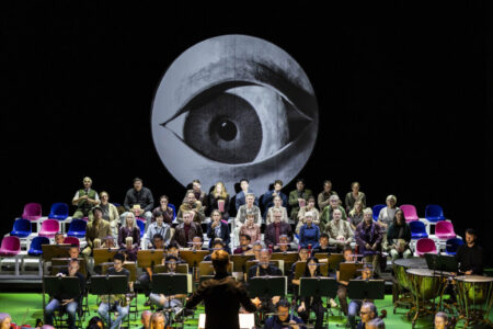 Romeo und Julia. Ein Tragödie in vier Künsten. Szenenfoto mit Damen und Herren des Opernchors und Mitgliedern des Philharmonischen Orchesters. Am Pult der Musikalische Leiter GMD Alexander Merzyn. Über allen in der Mondscheibe ein entsetztes Auge.